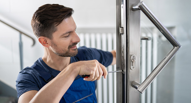 un serrurier de face réparant une serrure de porte en verre